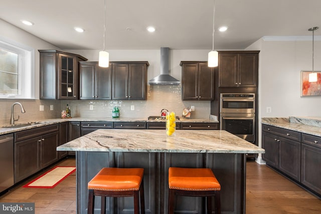 kitchen featuring dark wood-type flooring, hanging light fixtures, wall chimney exhaust hood, and sink