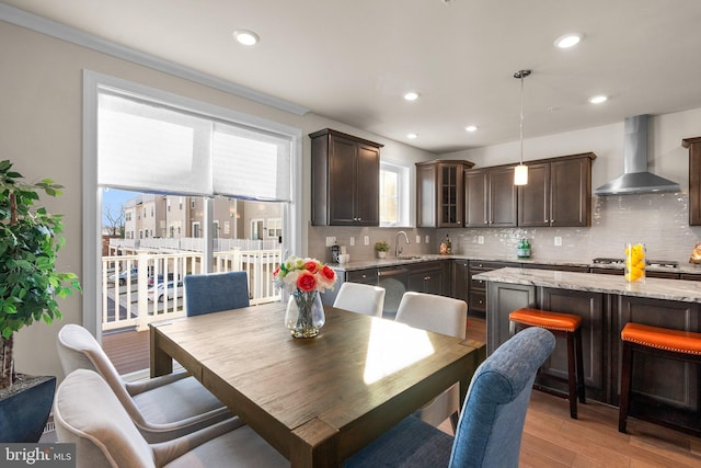 kitchen featuring backsplash, hanging light fixtures, wall chimney exhaust hood, light stone countertops, and light hardwood / wood-style floors