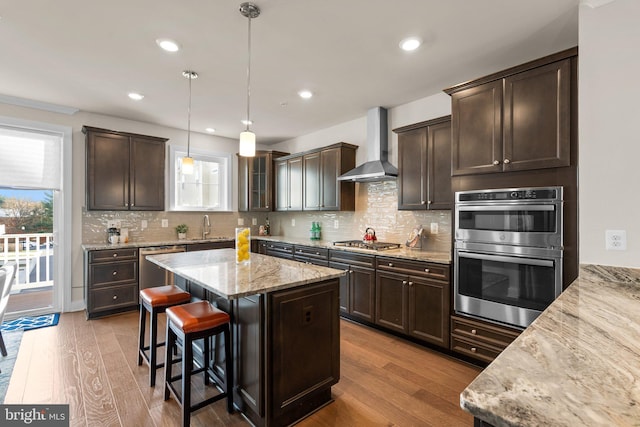 kitchen featuring hardwood / wood-style floors, stainless steel appliances, a wealth of natural light, and wall chimney range hood