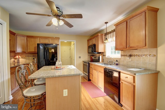 kitchen with pendant lighting, a center island, black appliances, sink, and light wood-type flooring