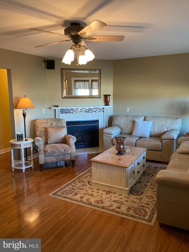 living room with ceiling fan, wood-type flooring, and a tile fireplace