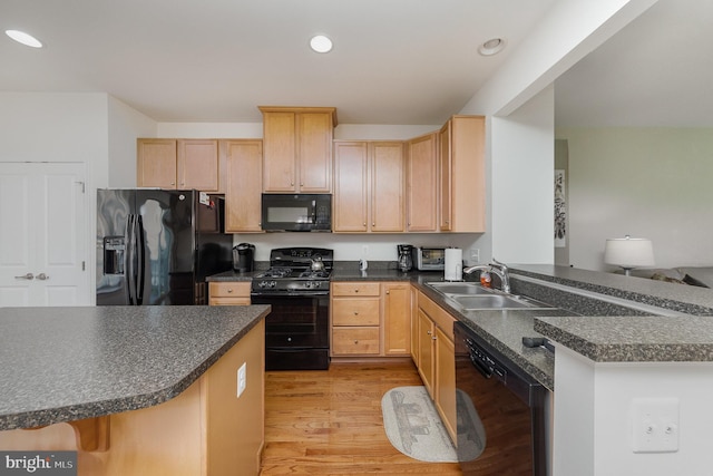 kitchen with kitchen peninsula, light brown cabinetry, light wood-type flooring, sink, and black appliances