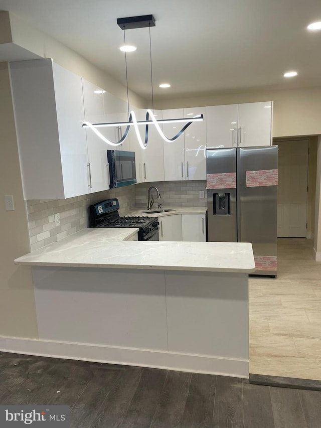 kitchen featuring pendant lighting, kitchen peninsula, white cabinetry, black range with gas cooktop, and stainless steel fridge