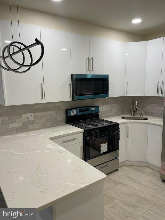 kitchen with light stone counters, sink, white cabinets, and gas range oven