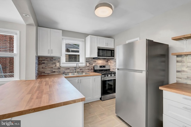 kitchen with butcher block counters, white cabinetry, sink, and stainless steel appliances