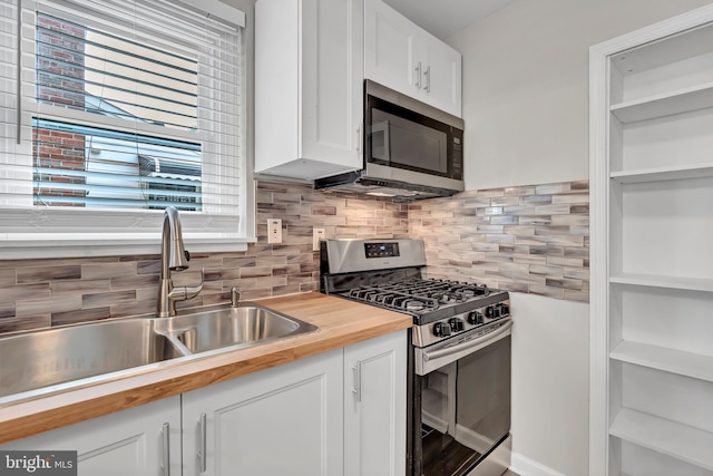 kitchen featuring appliances with stainless steel finishes, backsplash, sink, white cabinetry, and butcher block counters