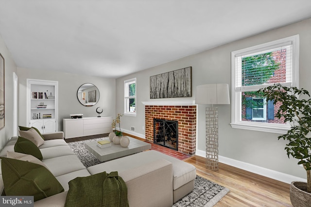 living room with built in features, light hardwood / wood-style floors, a brick fireplace, and plenty of natural light