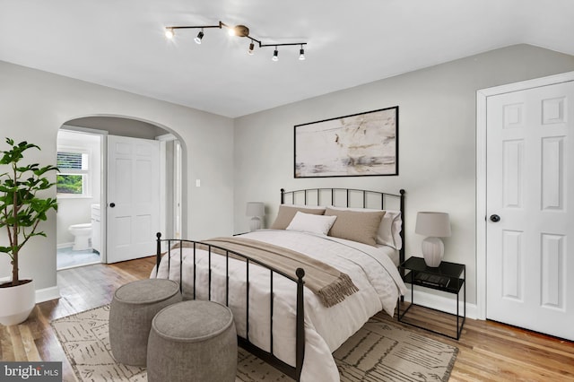 bedroom featuring ensuite bathroom, lofted ceiling, and light wood-type flooring