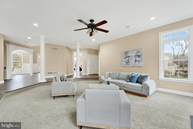 carpeted living room with decorative columns, ceiling fan, and a healthy amount of sunlight