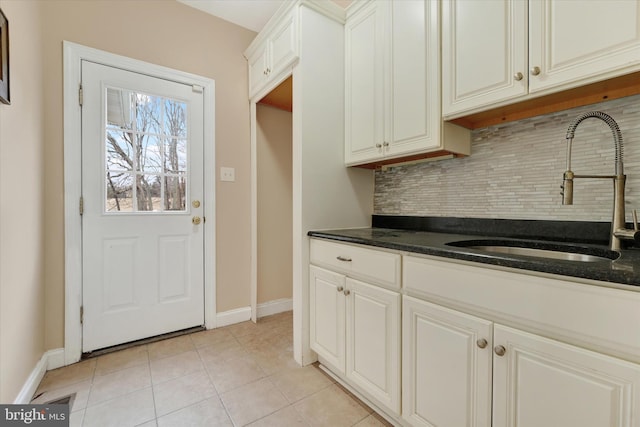 kitchen featuring decorative backsplash, sink, dark stone countertops, white cabinets, and light tile patterned flooring