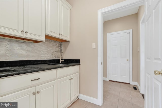 kitchen with backsplash, sink, light tile patterned floors, dark stone countertops, and white cabinetry