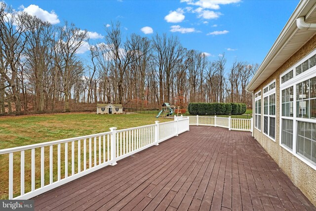 wooden terrace featuring a playground, a lawn, and a shed