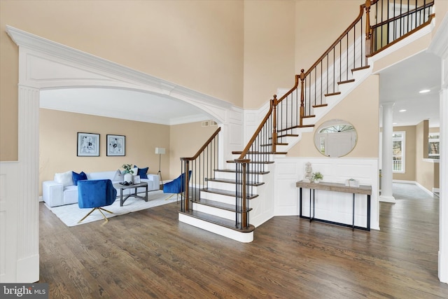 foyer entrance with decorative columns, crown molding, dark hardwood / wood-style flooring, and a high ceiling