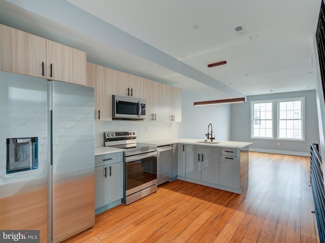 kitchen featuring pendant lighting, sink, decorative backsplash, kitchen peninsula, and stainless steel appliances