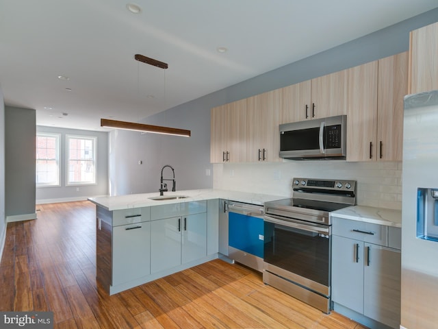 kitchen with kitchen peninsula, appliances with stainless steel finishes, light stone counters, sink, and light hardwood / wood-style flooring