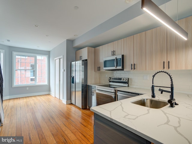 kitchen featuring sink, decorative backsplash, light stone countertops, appliances with stainless steel finishes, and light hardwood / wood-style floors