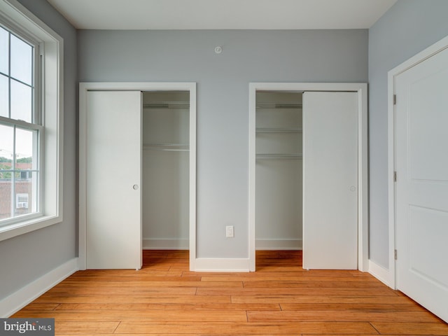 unfurnished bedroom with light hardwood / wood-style flooring and multiple closets