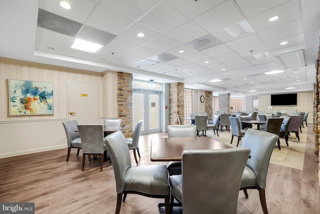 dining space with light wood finished floors, baseboards, a drop ceiling, and french doors