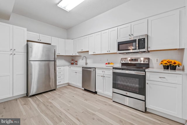 kitchen featuring stainless steel appliances, white cabinets, light countertops, and light wood-style flooring