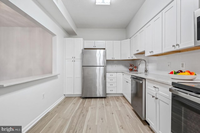 kitchen featuring tasteful backsplash, light wood-style flooring, stainless steel appliances, white cabinetry, and a sink