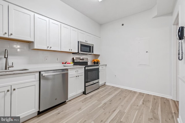 kitchen featuring light wood-style flooring, decorative backsplash, appliances with stainless steel finishes, white cabinetry, and a sink