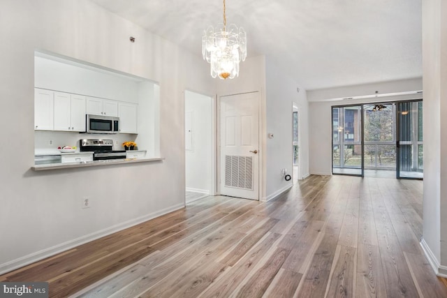 kitchen featuring baseboards, appliances with stainless steel finishes, open floor plan, wood finished floors, and white cabinetry