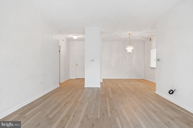 unfurnished living room featuring a chandelier, light wood-style flooring, and baseboards