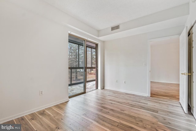 empty room with visible vents, a textured ceiling, light wood-style flooring, and baseboards