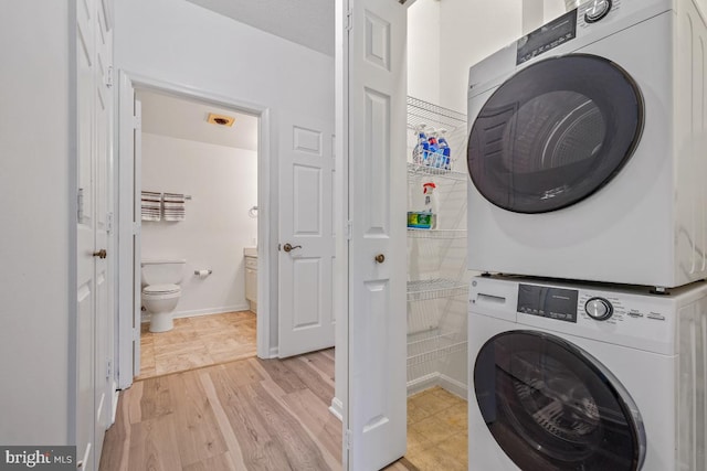 washroom with laundry area, light wood finished floors, stacked washing maching and dryer, and baseboards