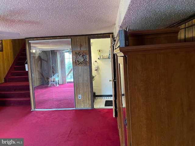 hall featuring carpet, a textured ceiling, and wooden walls