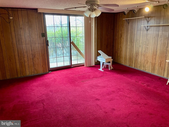 empty room with a textured ceiling, ceiling fan, and wood walls