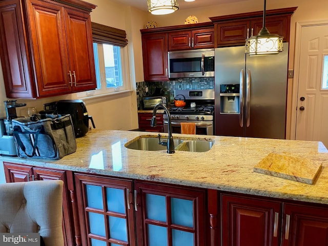 kitchen with sink, stainless steel appliances, light stone counters, backsplash, and pendant lighting