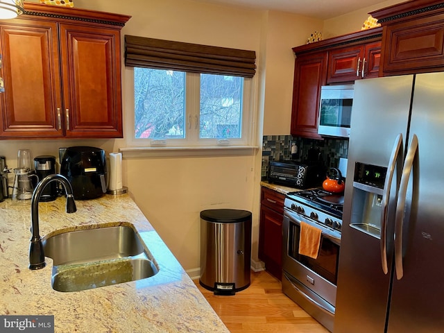 kitchen with light stone countertops, light wood-type flooring, backsplash, stainless steel appliances, and sink