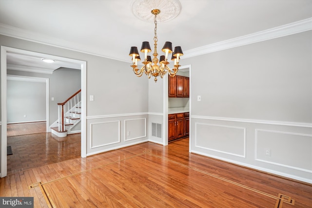 unfurnished dining area with a notable chandelier, crown molding, and hardwood / wood-style floors