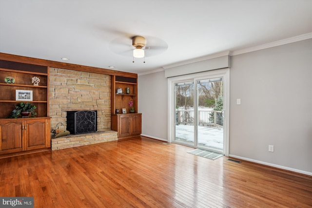 unfurnished living room with ceiling fan, built in shelves, a stone fireplace, and light wood-type flooring