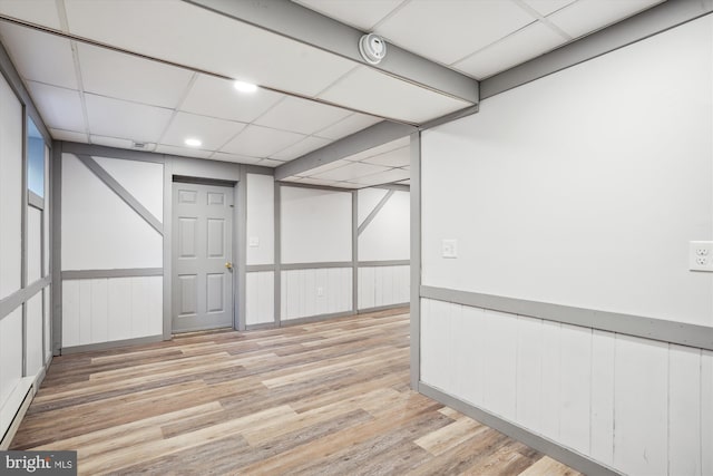 empty room featuring a drop ceiling, light hardwood / wood-style floors, and a baseboard heating unit