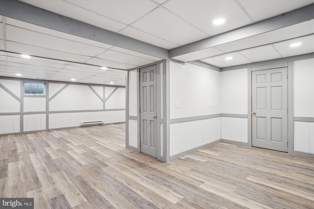 basement with a baseboard radiator, a drop ceiling, and light wood-type flooring