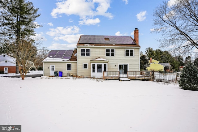 snow covered house with a deck and solar panels