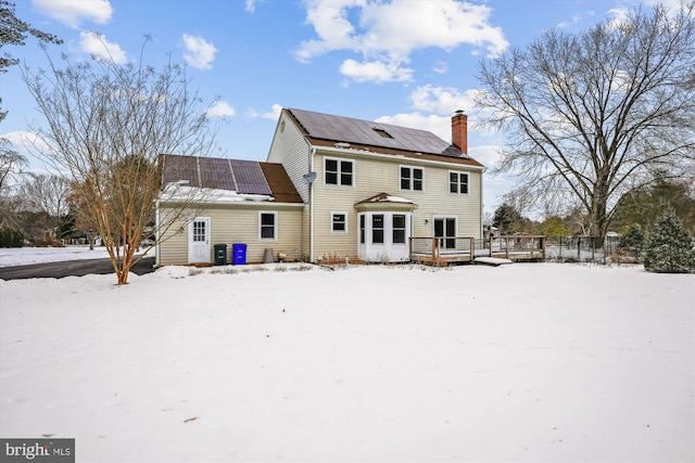 snow covered back of property with a deck and solar panels