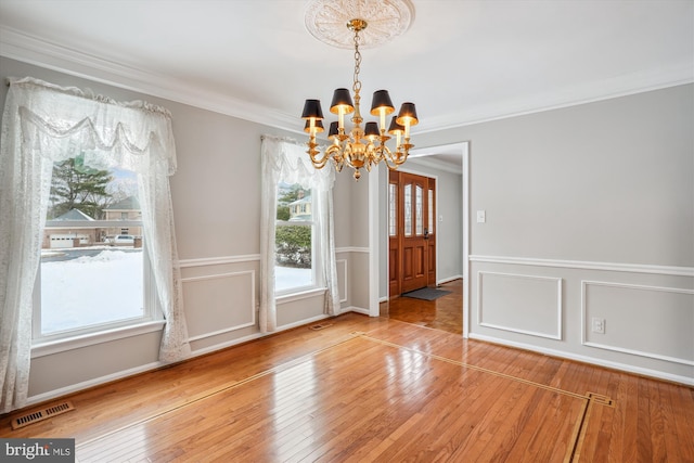 unfurnished dining area featuring crown molding, hardwood / wood-style flooring, and a notable chandelier