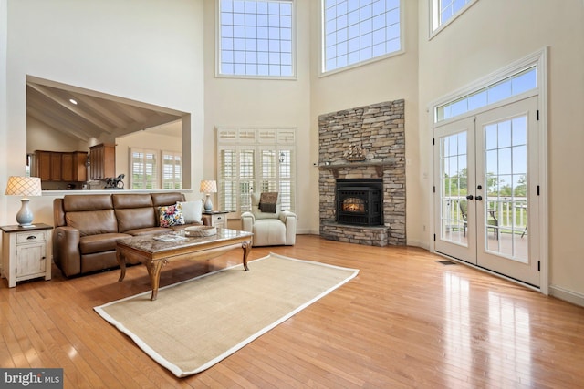 living room featuring french doors, a stone fireplace, a towering ceiling, and light hardwood / wood-style flooring