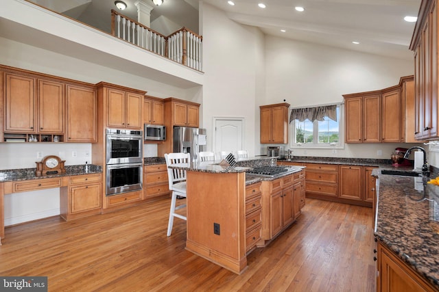 kitchen with sink, a breakfast bar area, appliances with stainless steel finishes, dark stone countertops, and a high ceiling