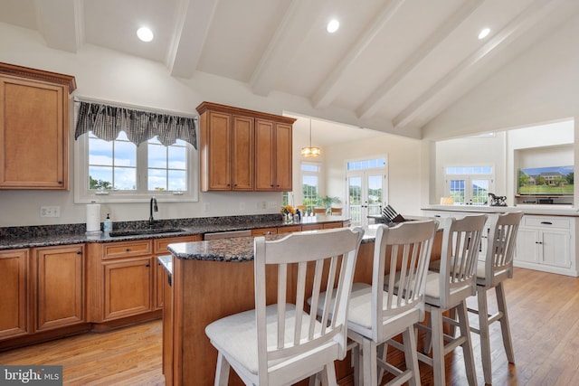 kitchen with sink, dark stone countertops, light hardwood / wood-style floors, a kitchen bar, and decorative light fixtures