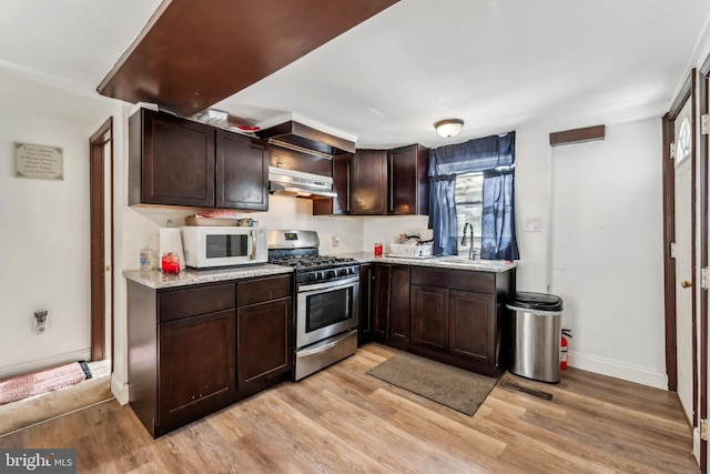 kitchen featuring white microwave, under cabinet range hood, dark brown cabinetry, and gas range