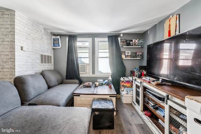 living area with brick wall, visible vents, and wood finished floors