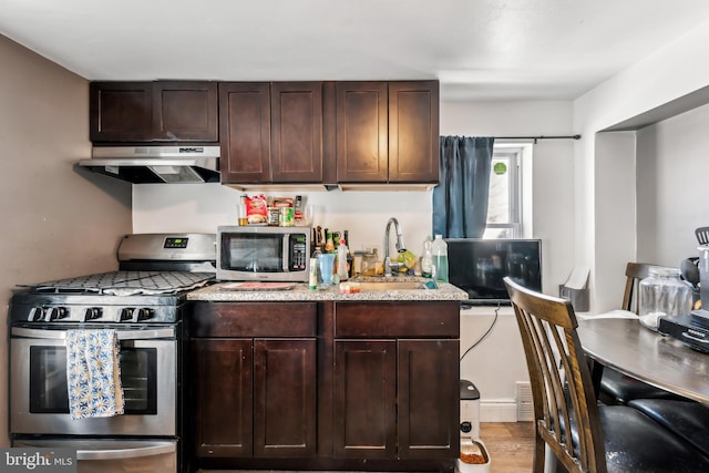 kitchen featuring light wood-style flooring, dark brown cabinetry, under cabinet range hood, stainless steel appliances, and a sink