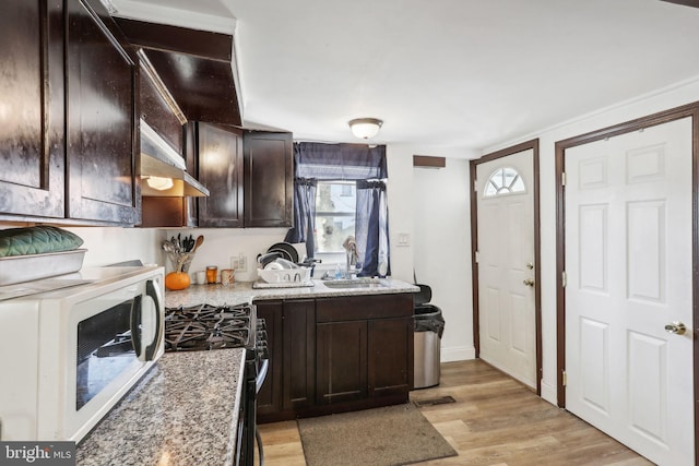 kitchen with light wood finished floors, gas range, dark brown cabinets, wall chimney range hood, and a sink