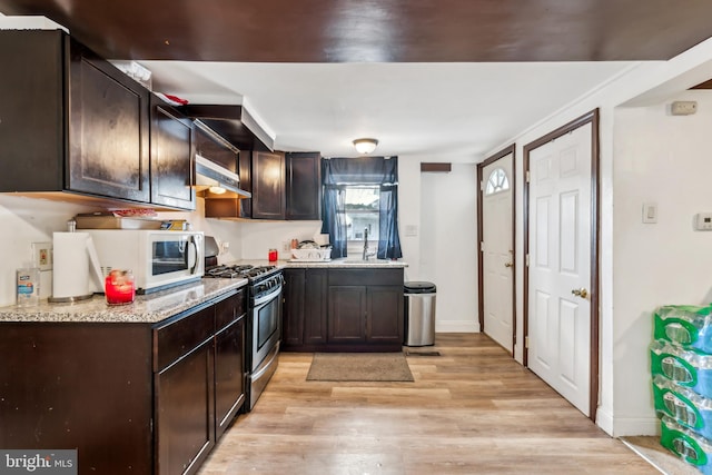 kitchen featuring stainless steel range with gas cooktop, white microwave, a sink, dark brown cabinetry, and wall chimney exhaust hood