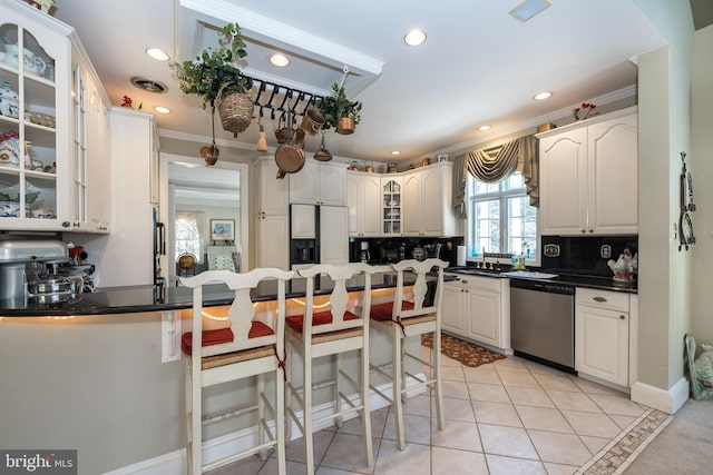 kitchen featuring a breakfast bar, crown molding, stainless steel dishwasher, decorative backsplash, and light tile patterned flooring