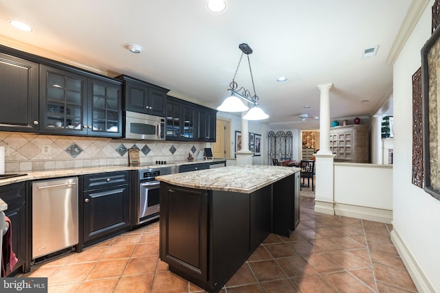 kitchen featuring ornate columns, backsplash, pendant lighting, a kitchen island, and appliances with stainless steel finishes